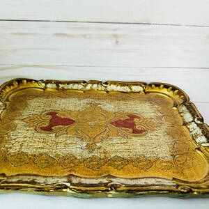 May include: A gold and white wooden tray with a decorative red and gold design. The tray has a scalloped edge and is perfect for serving snacks or drinks.