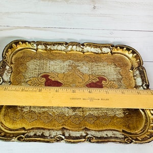 May include: A decorative tray with a gold and white finish and intricate floral designs. The tray has a scalloped edge and measures approximately 9 inches in length.