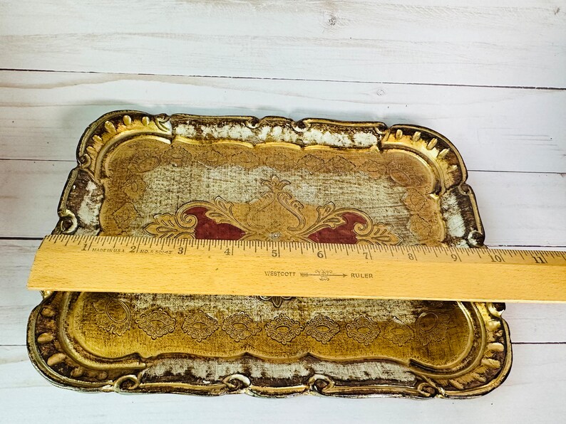 May include: A decorative tray with a gold and white finish and intricate floral designs. The tray has a scalloped edge and measures approximately 9 inches in length.