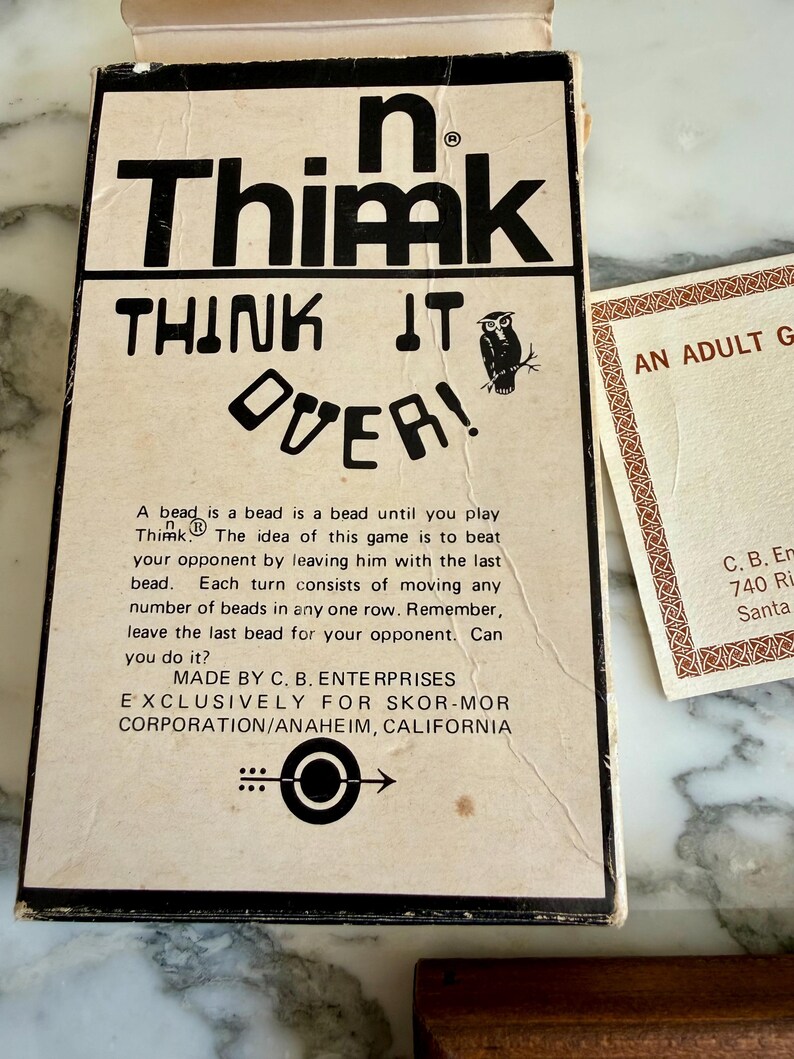 K&ouml;nnte beinhalten: Vintage "n Thimk" Brettspielbox mit fetter schwarzer Schrift und einer Eulenillustration. Auf der Box steht "THINK IT OVER!" und enth&auml;lt Spielanweisungen. Eine Karte mit dekorativen R&auml;ndern ist ebenfalls sichtbar.
