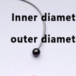 May include: A silver choker necklace with a black bead at each end. The inner diameter is around 6.6 cm, and the outer diameter is around 6.7 cm. The necklace is shown against a white backdrop.