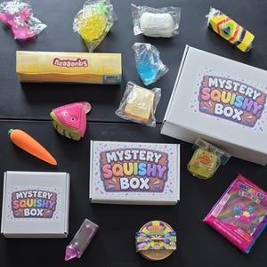 May include: A collection of various squishy toys in individual plastic packaging, including a carrot, a watermelon slice, and a long yellow box labeled Squeezy. Two white cardboard boxes are labeled Mystery Squishy Box with colorful text.