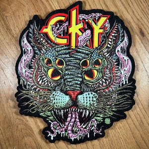 May include: A black and yellow patch with a cat-like creature with multiple eyes and a large mouth. The creature has a yellow and black "CKY" logo on its forehead. The patch is made of felt and has a stitched edge.