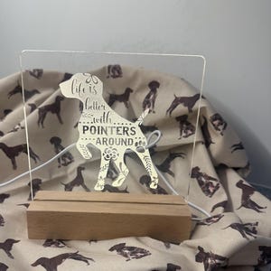 May include: A clear acrylic sign with a silhouette of a dog and the text "Life is better with pointers around". The sign is lit from behind and sits on a wooden base.