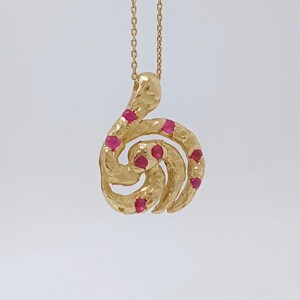 May include: Gold necklace with a pendant shaped like a swirl with red gemstones.