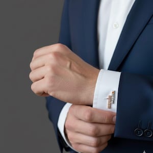 Peut inclure: Gros plan sur un costume bleu marine avec une chemise blanche et des boutons de manchette en or et argent. Les boutons de manchette ont un design rectangulaire avec de petits détails scintillants. La personne ajuste le poignet de la chemise.