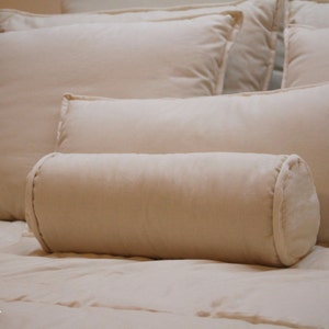 Può includere: Un letto bianco con un cuscino a rullo bianco e diversi cuscini bianchi. Il letto è fatto con lenzuola bianche e una coperta bianca.