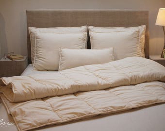 May include: A white duvet cover with a quilted design, on a bed with white pillows and a beige headboard.