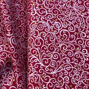 May include: Red fabric with a white and gold swirl pattern. The fabric has a repeating pattern of white swirls with gold stars scattered throughout.