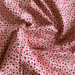May include: A piece of fabric featuring a dense, repeating pattern of small, multi-pointed stars in various shades of red, ranging from bright crimson to deep maroon, set against a clean, off-white background with soft, draped folds.