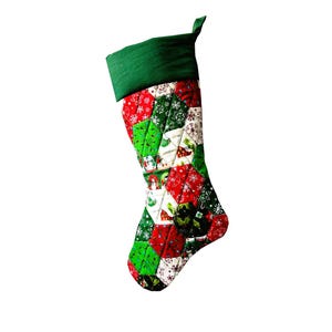 Könnte beinhalten: Ein gesteckter Weihnachtsstrumpf mit grünem Bund und Aufhängeschlaufe. Der Körper besteht aus roten, grünen und weißen Stoffquadraten, die mit Schneeflocken und festlichen Mustern verziert sind. Eine traditionelle Weihnachtsdekoration.