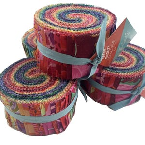 May include: Four rolls of colourful fabric strips, tightly wound and secured with light blue ribbon. The fabric features a vibrant mix of red, pink, purple, and yellow hues. Each roll has a tag that reads "Kaffe Fassett Collective".