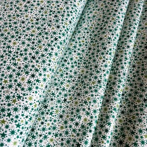 May include: A folded length of white fabric featuring a dense, repeating pattern of small stars in varying shades of dark green, light green, and grey. The stars are rendered in different sizes and styles, creating a textured, celestial-inspired print.