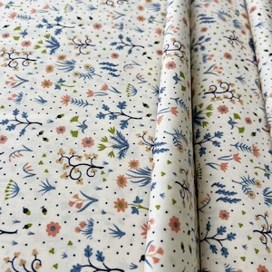 Könnte beinhalten: Weißer Stoff mit einem sich wiederholenden Blumenmuster. Das Design zeigt blaue, pfirsichfarbene und grüne Blumen und Blätter sowie kleine schwarze Punkte. Der Stoff ist gefaltet und zeigt die Wiederholung des Musters.