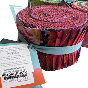 May include: Fabric rolls in shades of pink, red, and purple are bundled with a light blue ribbon. The rolls are labelled "FB4DRGP.RUBY" and are made of 100% cotton. Each roll is approximately 6.35 cm in diameter.