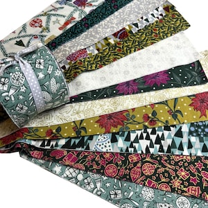 Può includere: Una collezione di strisce di tessuto a tema natalizio e una piccola scatola regalo. Le strisce di tessuto presentano vari motivi festivi, tra cui ornamenti, stelle e disegni botanici nei toni del verde, rosso e bianco. La scatola regalo è verde acqua con un nastro bianco.