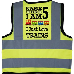 May include: Yellow and grey safety vest with reflective stripes. The vest has a black patch with the text "NAME HERE I AM 5 I JUST LOVE TRAINS" and a row of colourful toy train images.