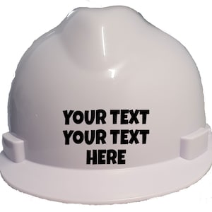 May include: A white hard hat with a smooth, glossy finish and a rounded crown. The front of the hard hat features the black printed text "YOUR TEXT YOUR TEXT HERE" in a bold, sans-serif font, centred on the surface of the protective headgear.
