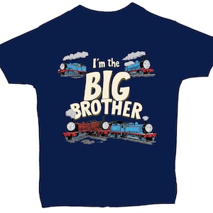 Peut inclure: T-shirt bleu marine avec l'inscription "I'm the BIG BROTHER" et des illustrations de trains de dessins animés. Les trains sont bleus et rouges, avec des panaches de fumée blanche.