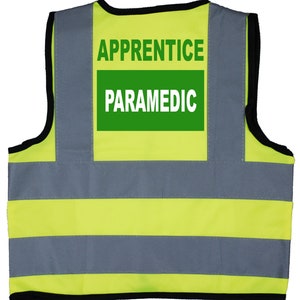 Könnte beinhalten: Gelbe und graue Sicherheitsweste mit reflektierenden Streifen. Die Weste hat einen grünen Aufnäher mit der Aufschrift "APPRENTICE PARAMEDIC".