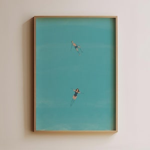 Może przedstawiać: Wydruk w ramie przedstawiający turkusowy ocean z dwoma postaciami pływającymi w wodzie. Wydruk wisi na białej ścianie, a na pierwszym planie znajduje się drewniane krzesło.