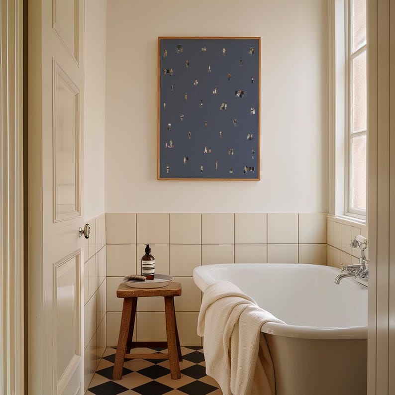 May include: A rectangular wall art print featuring a dark blue background with a scattered pattern of tiny, diverse human figures. The artwork is framed in a thin, light-toned wood frame and is displayed on a cream-colored wall above a bathtub.