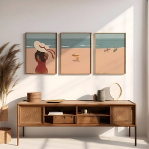 May include: Three framed illustrations of a beach scene. The first illustration shows a person in a red swimsuit and a white hat standing on the beach. The second illustration shows a beach umbrella and a beach chair on the sand. The third illustration shows two people surfing in the ocean.