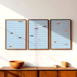 May include: Three framed prints of a blue and white striped pattern with figures of people swimming in a pool. The prints are hung on a white wall above a wooden cabinet.