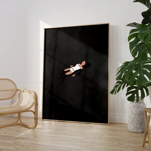 May include: A framed wall art print featuring a minimalist illustration of a figure floating in a vast, solid black space. The figure is depicted in a white top and white bottoms, with dark hair, positioned centrally against the deep black background.