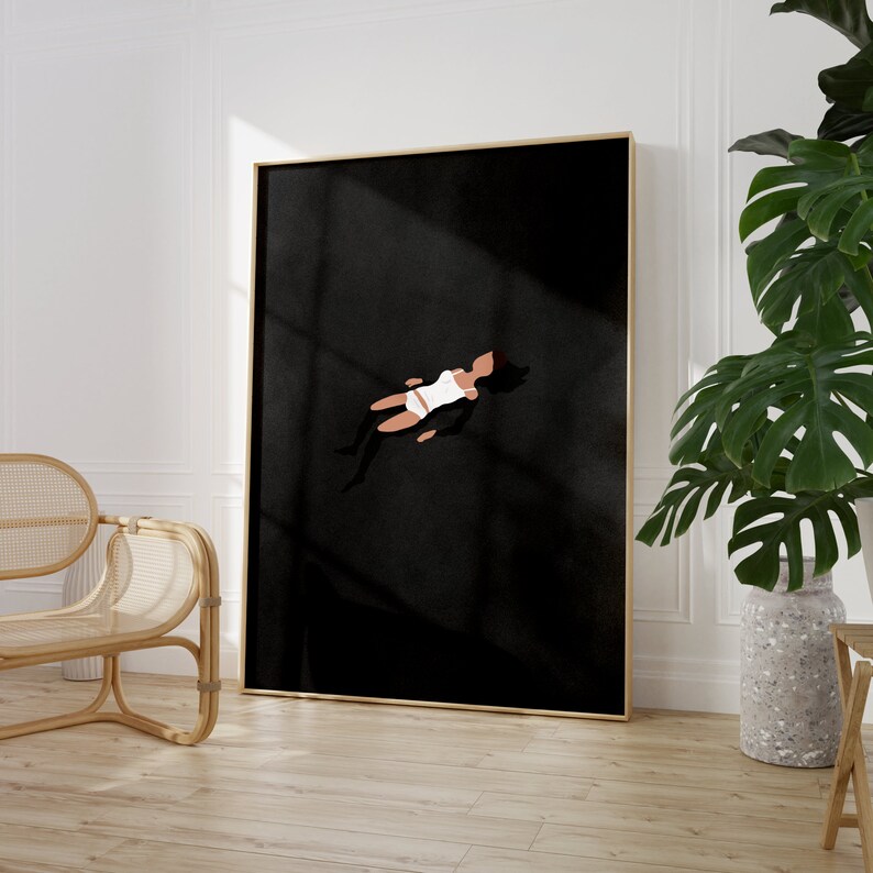 May include: A framed wall art print featuring a minimalist illustration of a figure floating in a vast, solid black space. The figure is depicted in a white top and white bottoms, with dark hair, positioned centrally against the deep black background.