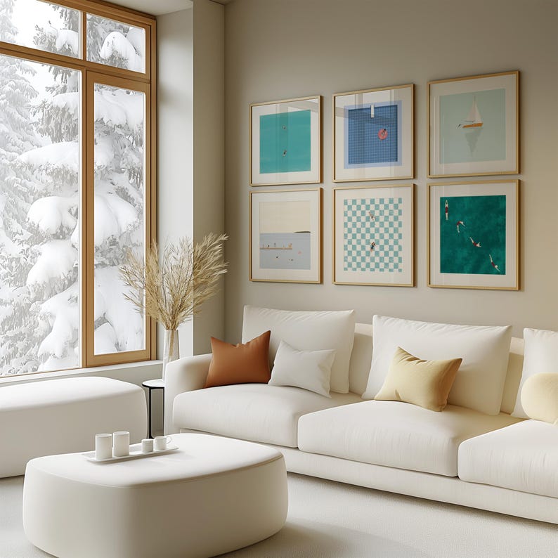 K&ouml;nnte beinhalten: Ein wei&szlig;es Sofa mit braunen und cremefarbenen Kissen steht vor einer Wand mit einer Galerie gerahmter Kunstwerke. Die Kunstwerke zeigen abstrakte Designs in Blaut&ouml;nen, Gr&uuml;nt&ouml;nen und Wei&szlig;. Ein gro&szlig;es Fenster hinter dem Sofa zeigt eine verschneite Winterlandschaft.