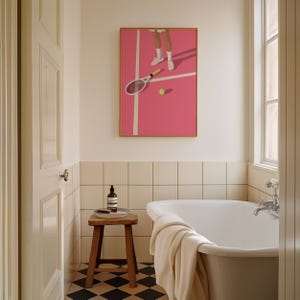 May include: A white bathtub with a white towel on the side, a small wooden stool with a bottle of soap and a tray on top, and a framed print of a tennis player on a pink court above the bathtub.