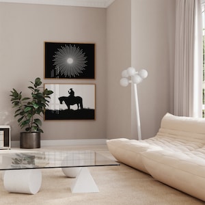 May include: A living room interior with a white sofa, a glass coffee table with white cylindrical and triangular bases, a potted plant, and two black and white framed prints on the wall.