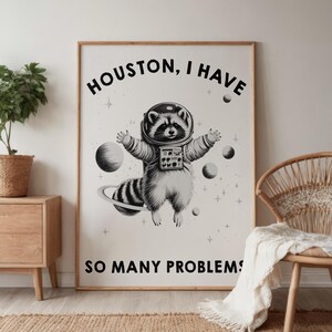 May include: A rectangular wall poster featuring a black and white illustration of a raccoon wearing a space helmet and suit, floating among planets and stars. The text reads HOUSTON, I HAVE SO MANY PROBLEMS in bold black capital letters.