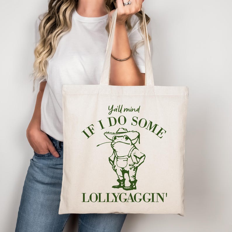 May include: A white canvas tote bag with a green frog illustration and the text "Y'all mind if I do some lollygaggin'"
