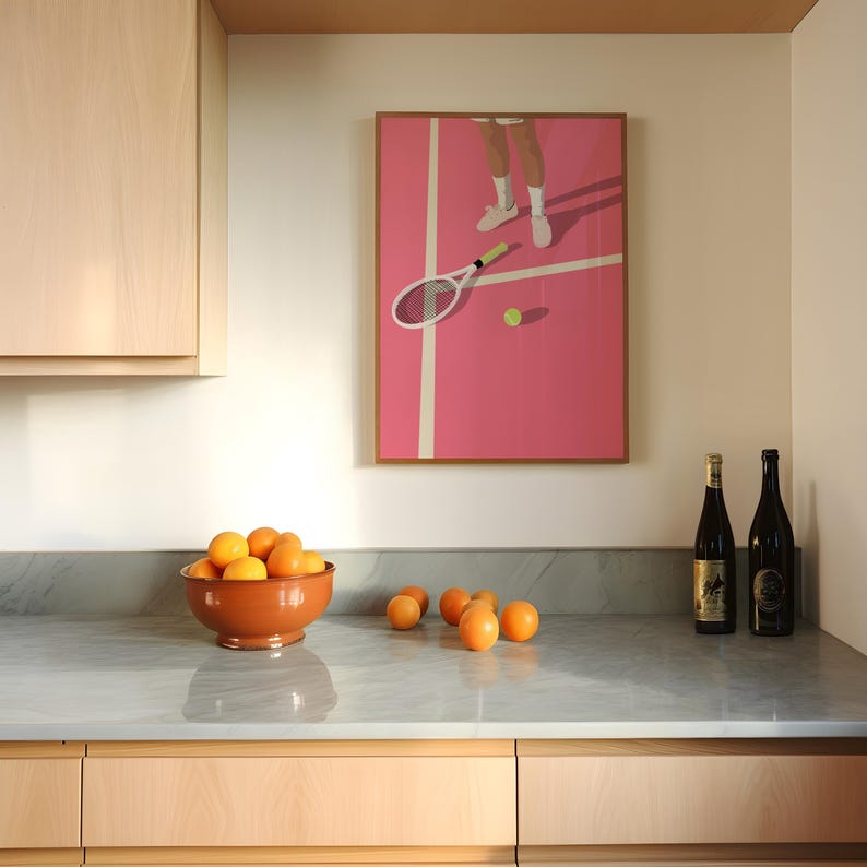 May include: A kitchen counter with a bowl of oranges, two bottles of wine, and a framed print of a tennis player on a pink court.