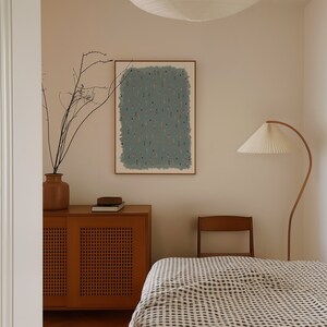 May include: A bedroom interior with a wooden cabinet, a bed with a white and black checkered duvet, a chair, and a floor lamp. A framed print with a blue background and a pattern of small red and white figures hangs on the wall.