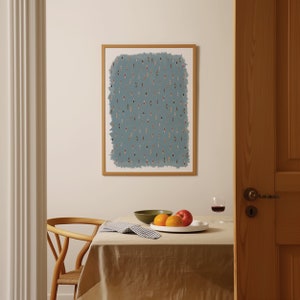 May include: A framed print of a blue background with a pattern of small, colorful figures. The print is hanging on a white wall above a table with a white tablecloth, a bowl of fruit, and a glass of wine.