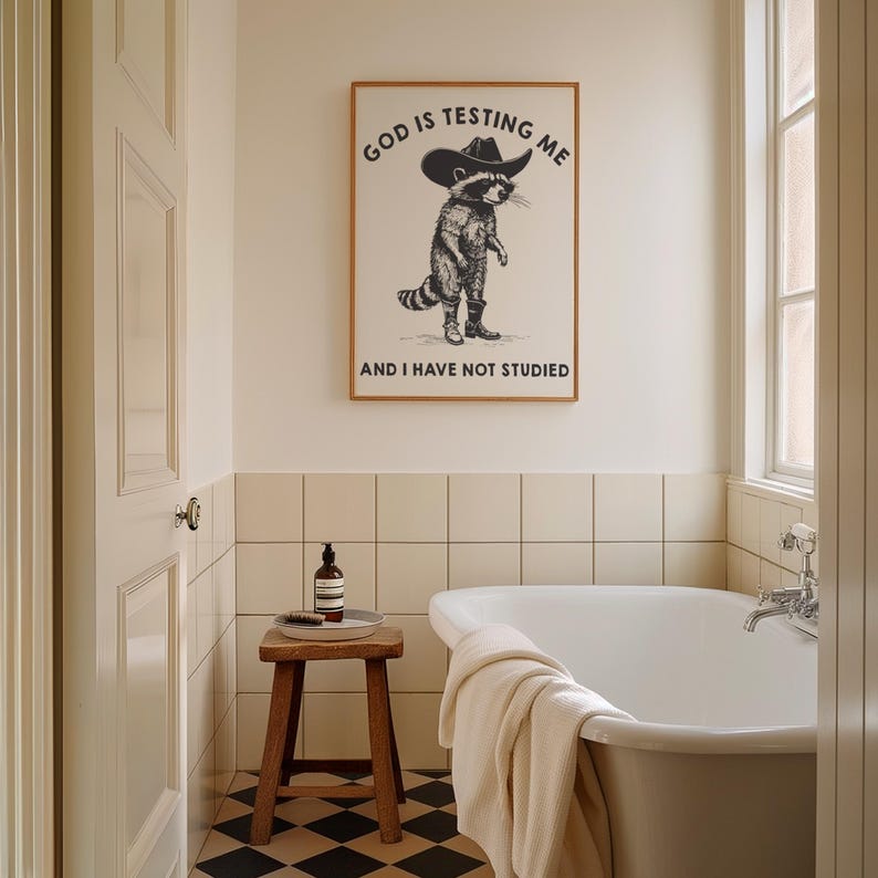 Puede incluir: Interior de ba&ntilde;o con un cuadro enmarcado que representa un mapache con sombrero y botas de vaquero, con el texto "GOD IS TESTING ME AND I HAVE NOT STUDIED". La habitaci&oacute;n incluye una ba&ntilde;era blanca, un taburete de madera y un suelo ajedrezado en blanco y negro.