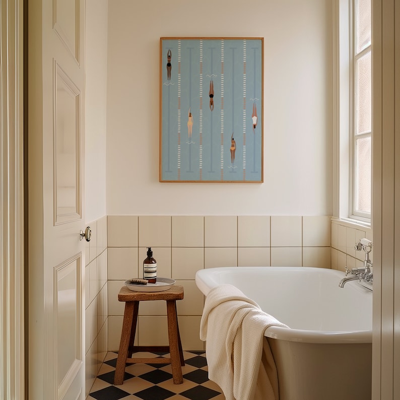 May include: A white bathtub with a white towel on the side, a wooden stool with a bottle of soap and a plate on top, and a framed print of swimmers in a pool on the wall above the bathtub.