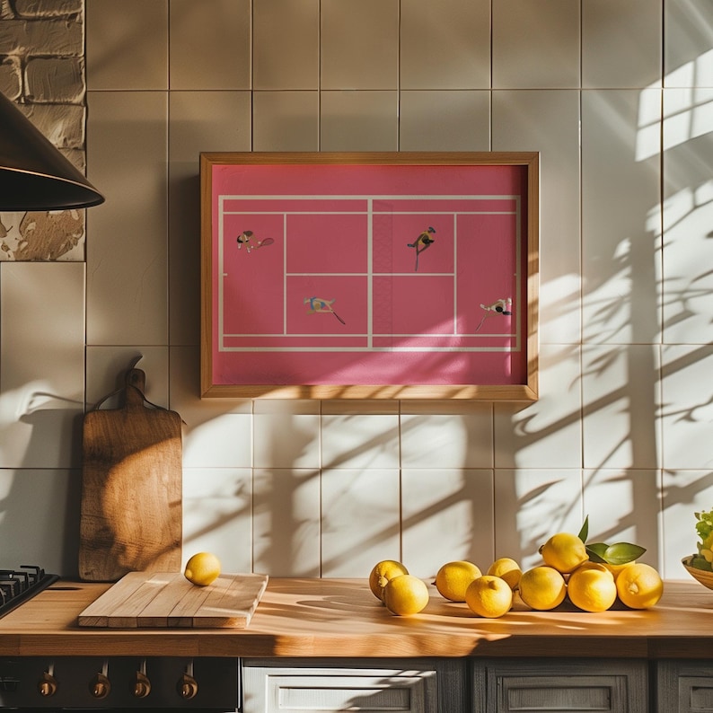 May include: A framed pink and white artwork with a tennis court design and small birds in flight. The artwork is hanging on a white tiled wall in a kitchen with a wooden countertop and lemons on the counter.