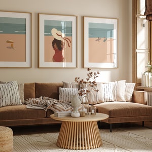 May include: Three framed illustrations of beach scenes. The leftmost illustration shows a beach with an umbrella and a drink. The middle illustration shows a woman in a hat and a red dress. The rightmost illustration shows two people surfing.