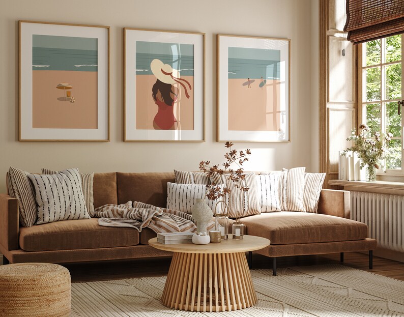 May include: Three framed illustrations of beach scenes. The leftmost illustration shows a beach with an umbrella and a drink. The middle illustration shows a woman in a hat and a red dress. The rightmost illustration shows two people surfing.