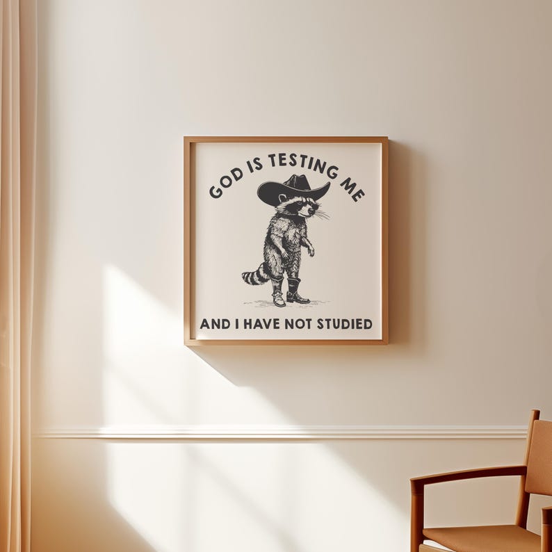 Puede incluir: Un estampado enmarcado con una ilustraci&oacute;n en blanco y negro de un mapache con sombrero de vaquero y botas. El texto encima del mapache dice "GOD IS TESTING ME" y debajo "AND I HAVE NOT STUDIED".