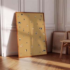 May include: A framed art print featuring a mustard-colored background with numerous tiny figures. The figures are depicted in various poses, suggesting a crowd or gathering. The frame is a warm brown color, and the artwork is leaning against a wall.
