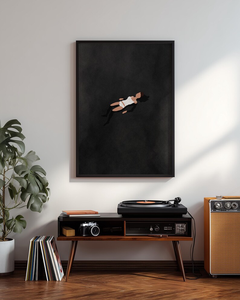 May include: A framed wall art print featuring a minimalist illustration of a figure floating in a dark, solid black void. The figure is depicted in a simplified style, wearing a white top and white bottoms, with dark hair against the black background.