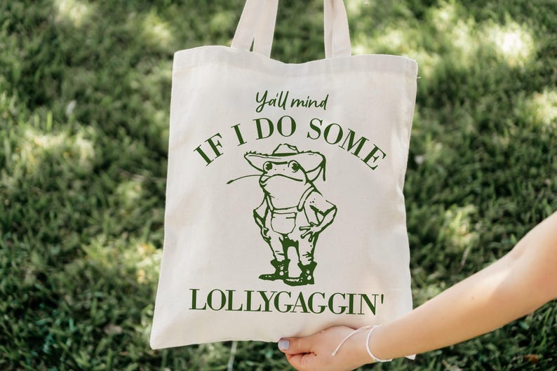 May include: A white canvas tote bag with green text that reads "Y'all mind if I do some lollygaggin'" and a cartoon frog wearing a hat and overalls.
