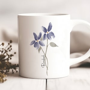 May include: White ceramic mug with a watercolor design of two purple flowers and the name "Rachel" written in cursive.