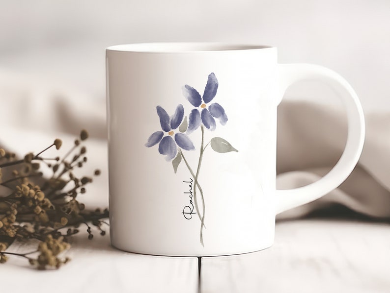 May include: White ceramic mug with a watercolor design of two purple flowers and the name "Rachel" written in cursive.