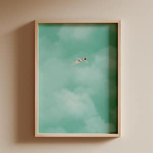 May include: A framed print of a woman swimming in a turquoise blue sky with white clouds. The woman is wearing a dark blue swimsuit.